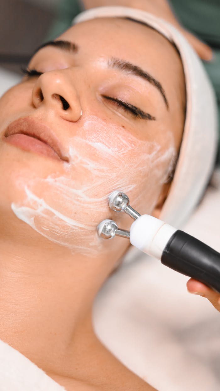 Close-up of a woman getting a facial treatment with a massager and face cream in a spa setting.